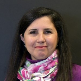 nicoletti bellinger headshot, lady with long dark hair, purple top and pink and white scarf in front of black background