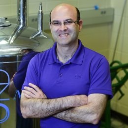 man with glasses wearing royal blue polo shirt with arms folded in science lab