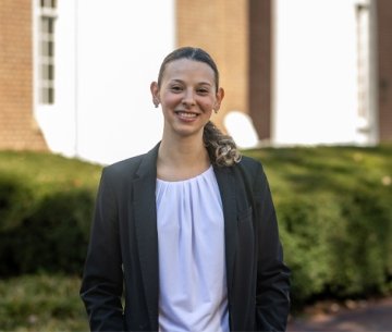 Student wearing sport coat and white top and smiling at camera