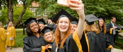 multiple students leaning in for a selfie photo in graduation attire