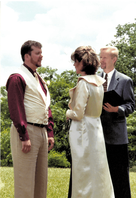 A groop, bride and wedding officiant stand in a field during a marriage ceremony. 