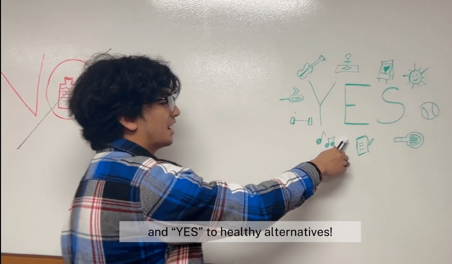 A student points to the word "yes" written on a dry erase board. 