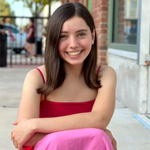 Lady with long dark hair wearing red and pink dress sitting on stairs