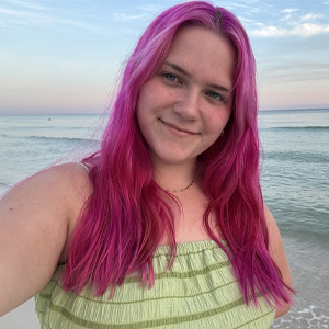 Lady with dyed pink red hair with green top standing in front of ocean
