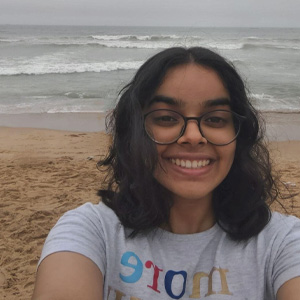 Lady with short dark hair wearing glasses standing in front of ocean waves on beach