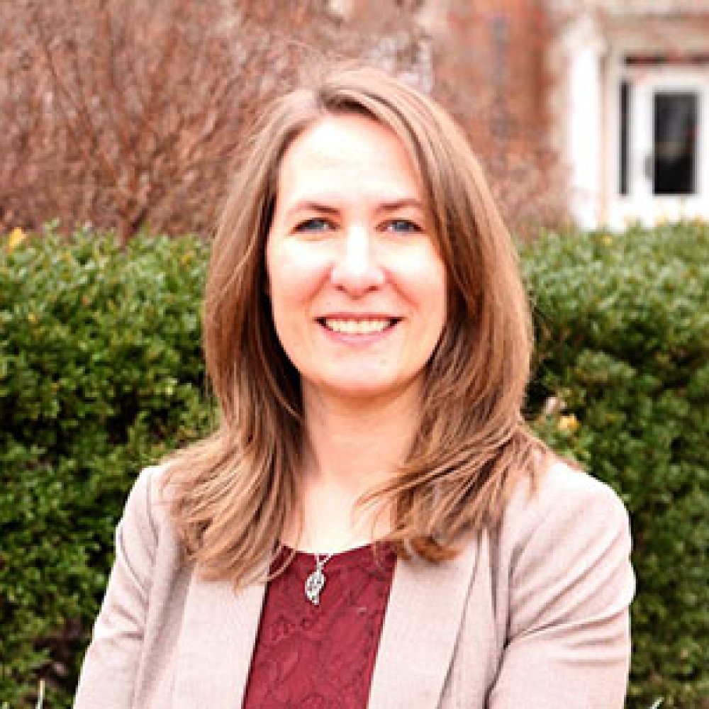 Lady with shoulder length brown hair wearing beige jacket and red top