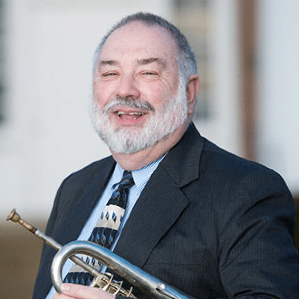 Person smiling while holding trumpet under their arm