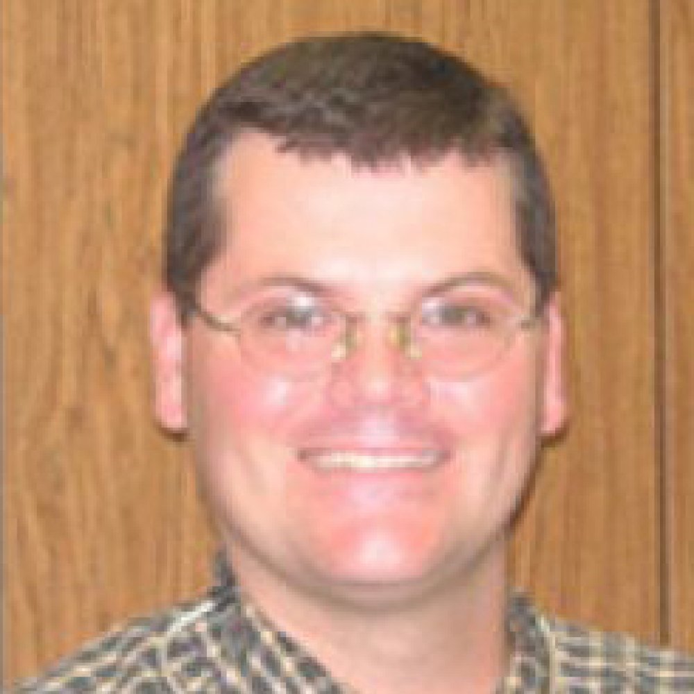 Man with dark hair and glasses wearing plaid grey and yellow shirt with stethoscope around neck