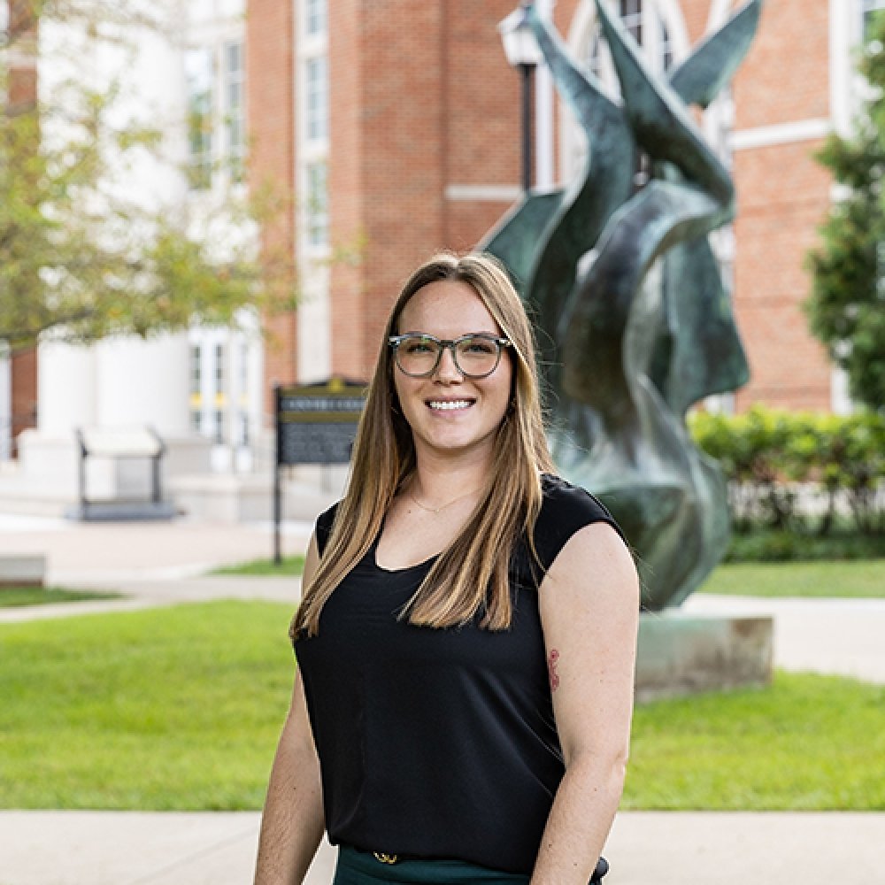 Lady with long brown hair wearing black top standing in front of flame statue