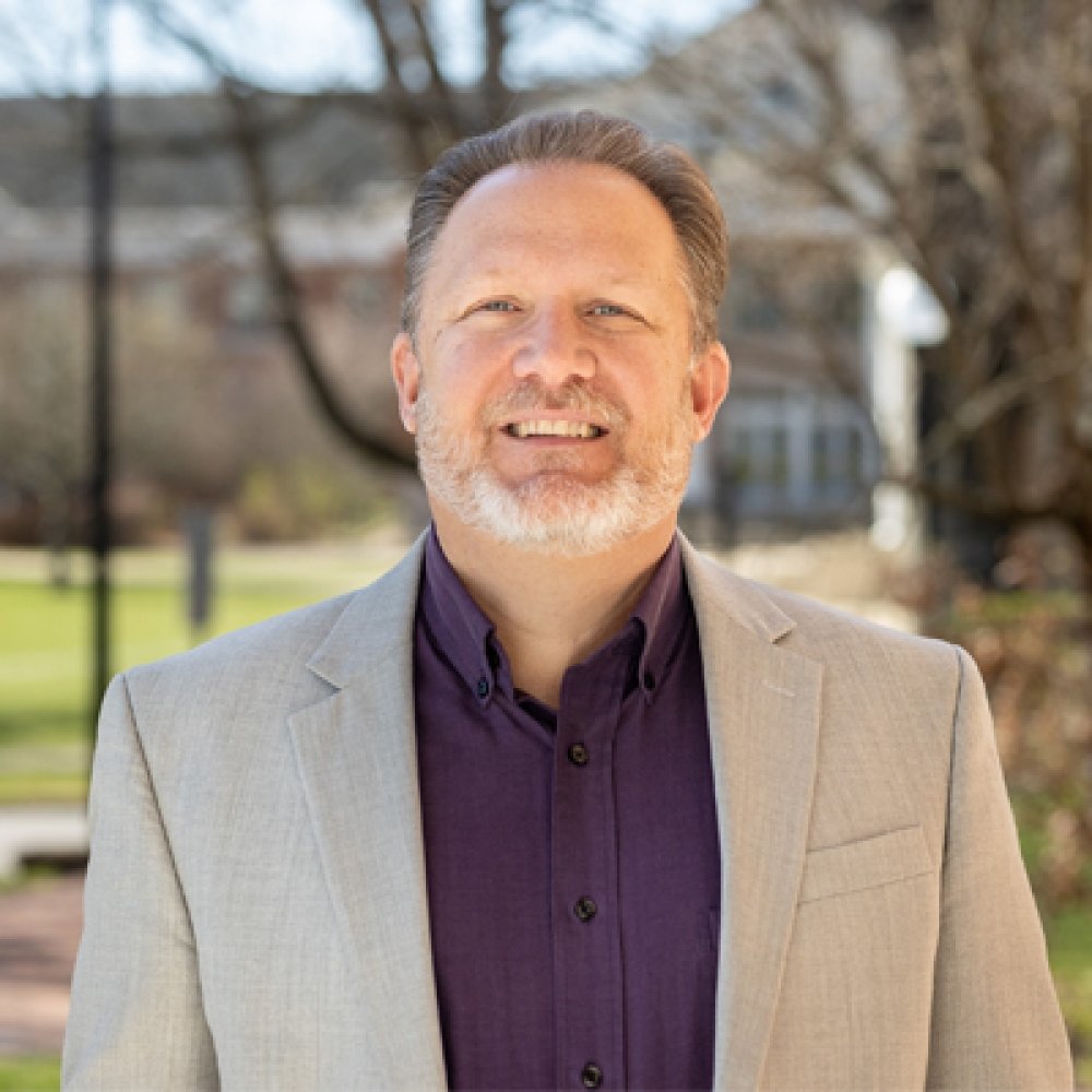 Person with beard wearing suit and smiling