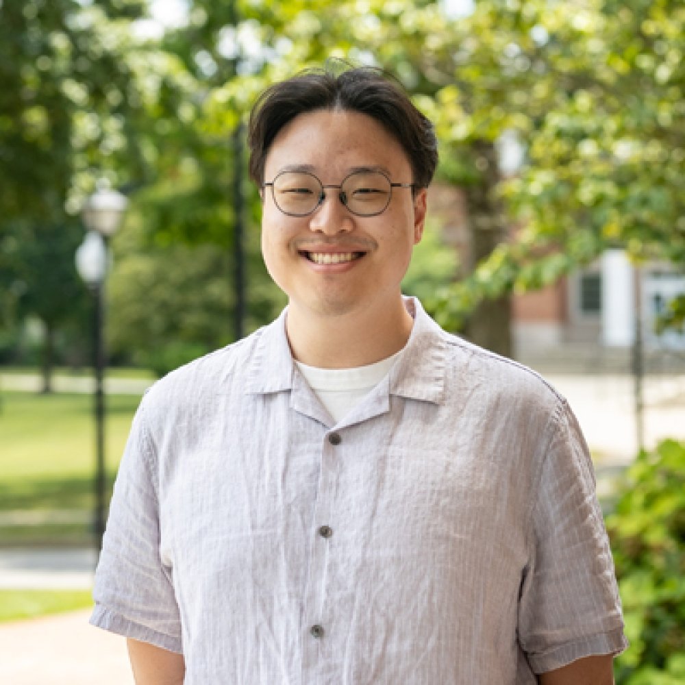 Person wearing button up short sleeve shirt with glasses, and smiling at camera