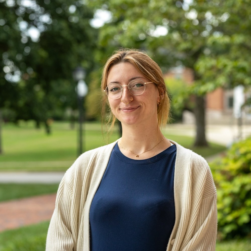 Person wearing glasses and blue top with camel cardigan and smiling at camera