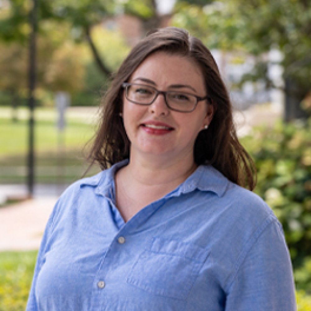 Person wearing blue button up shirt and glasses and smiling at camera