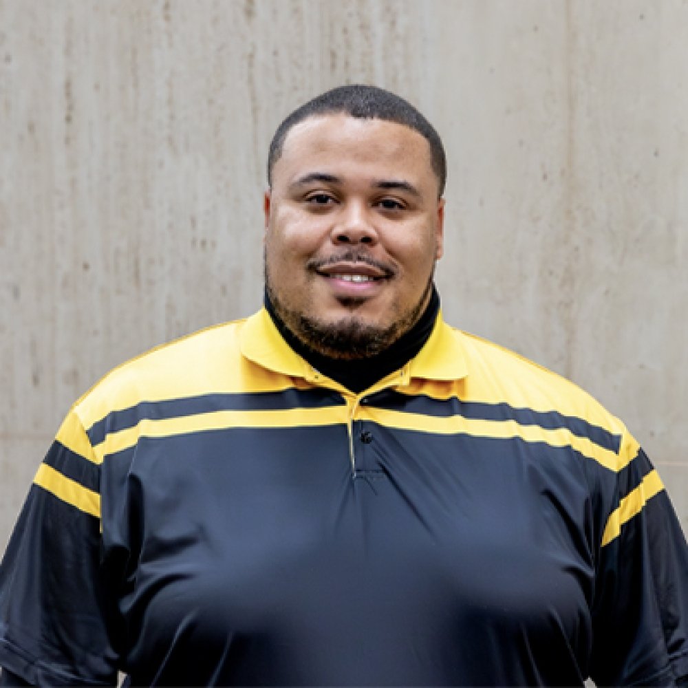 Person wearing gold and black polo top with DPS badge logo