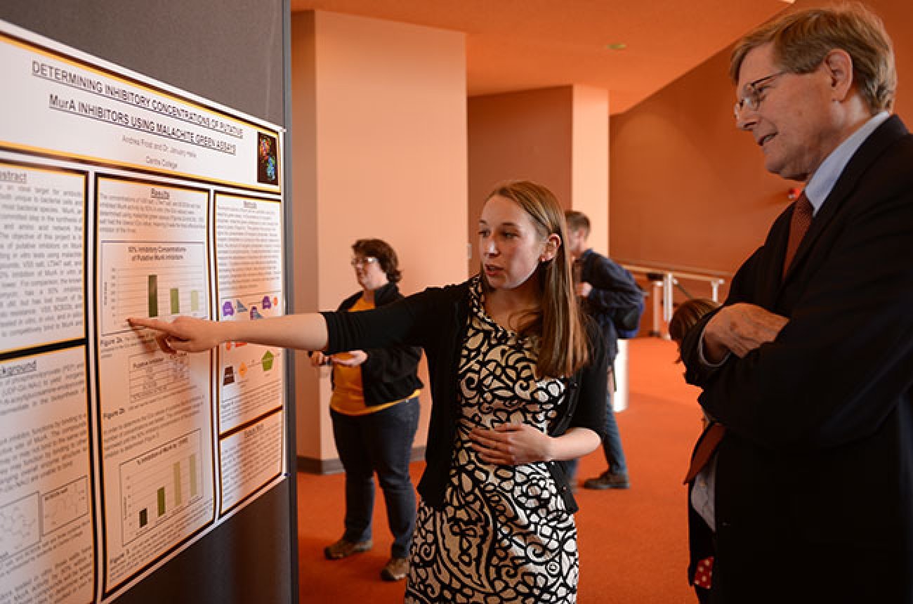 Student explaining study results in front of large poster display to faculty