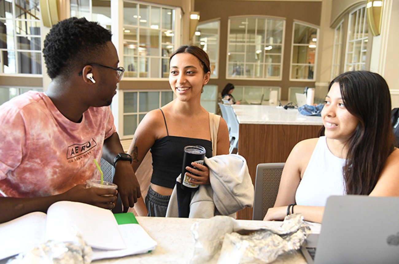 Three students speaking to each other inside the library taking a break from studying