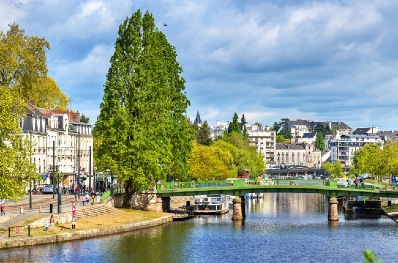 Park with older buildings, pond, trees, small bridge over pond in Nantes, France