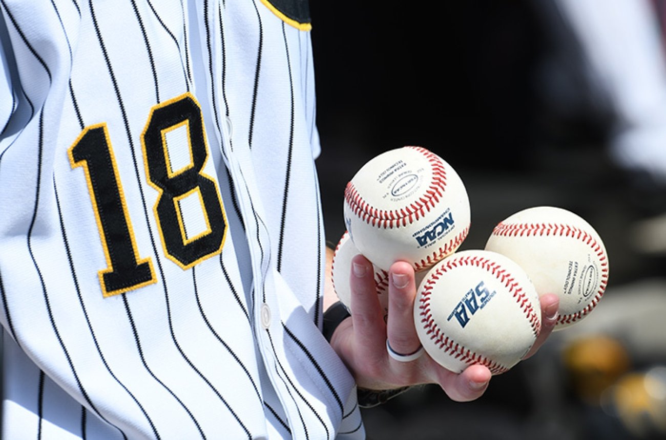 baseball player holding three Centre NCAA branded baseballs