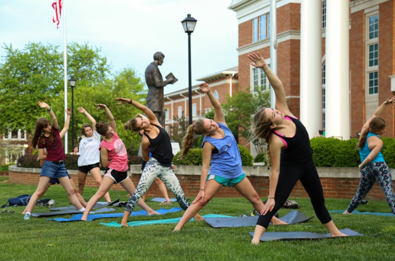 seven female students participating in yoga on the lawn in front of crounse with Abraham Lincoln statue in the background