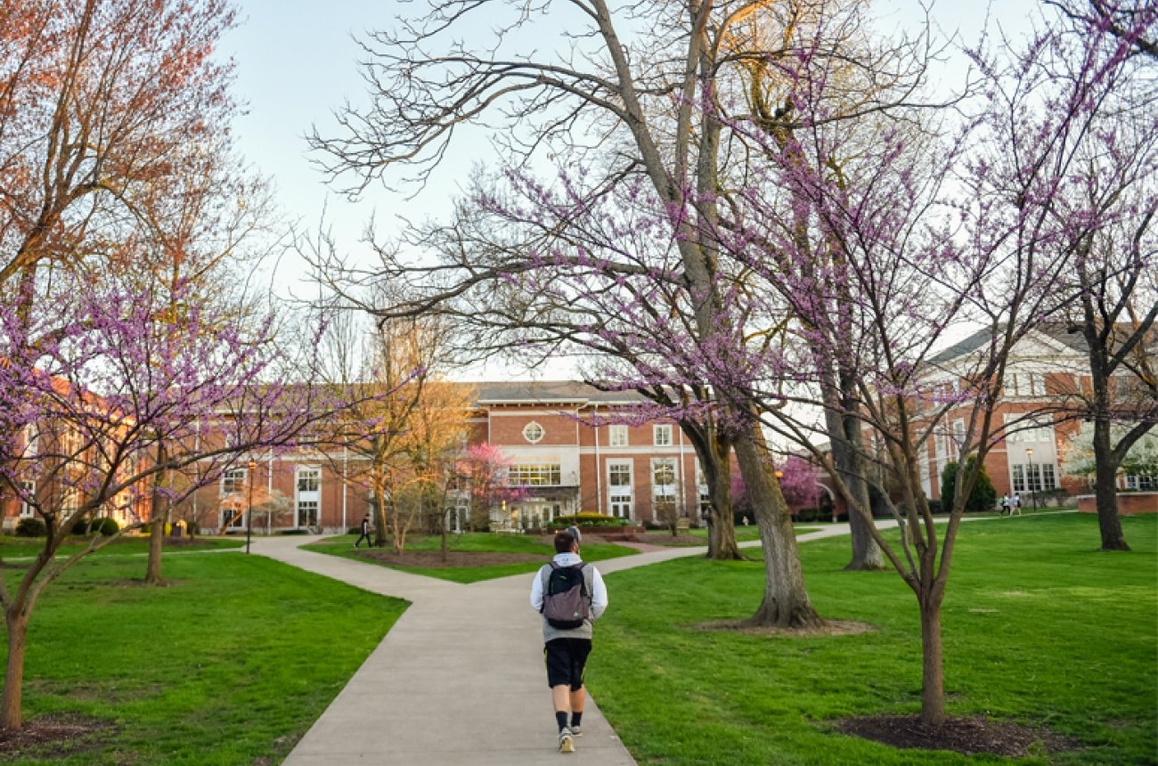 Student walking on sidewalk near campus building in spring
