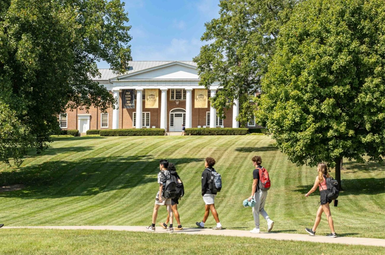 Four Students walking across campus in the spring, Old Centre in the background with graduation banners
