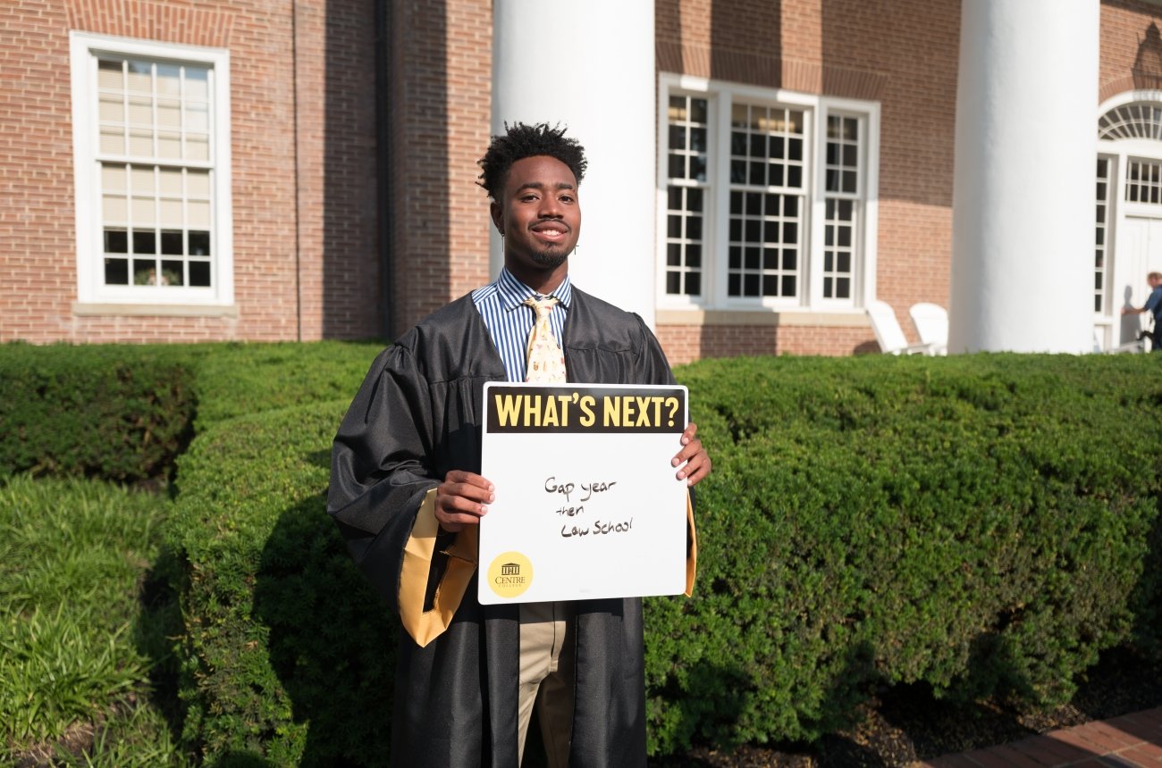 A graduating student holds a sign that reads &quot;What's next? Gap year and then law school&quot;