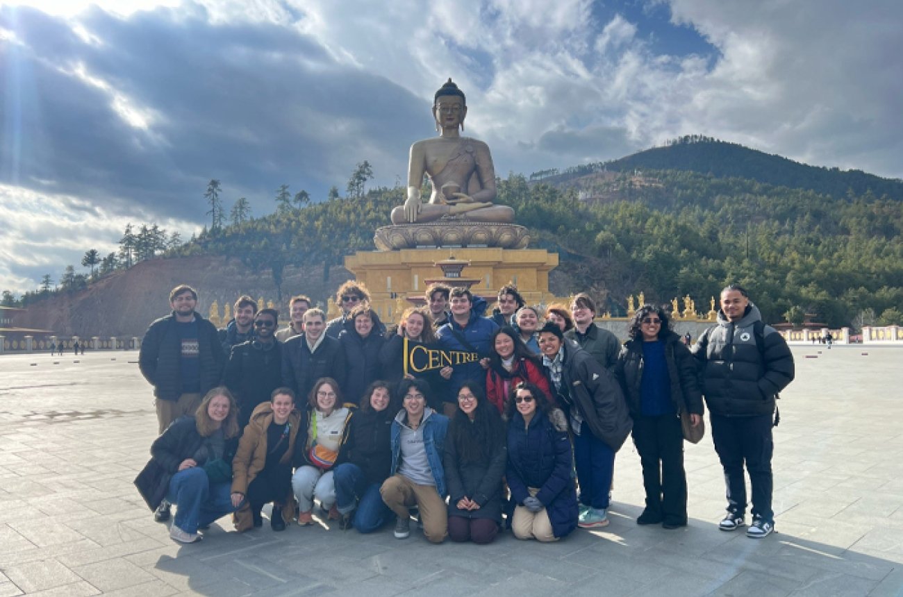 large group of students standing in front of Buddha statue