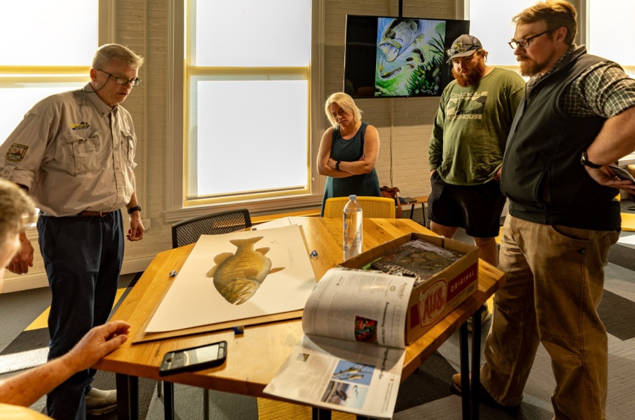 faculty and students looking at table with fishing illustration on it