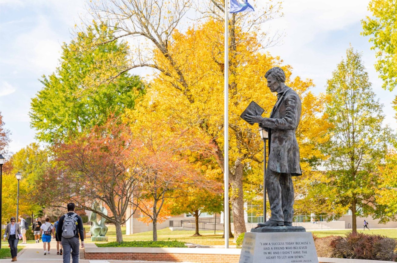 Students walking by Lincoln statue outside the library during fall
