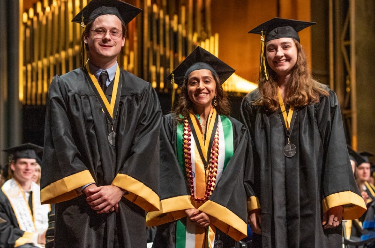 Students pose for photo in cap and gown at graduation