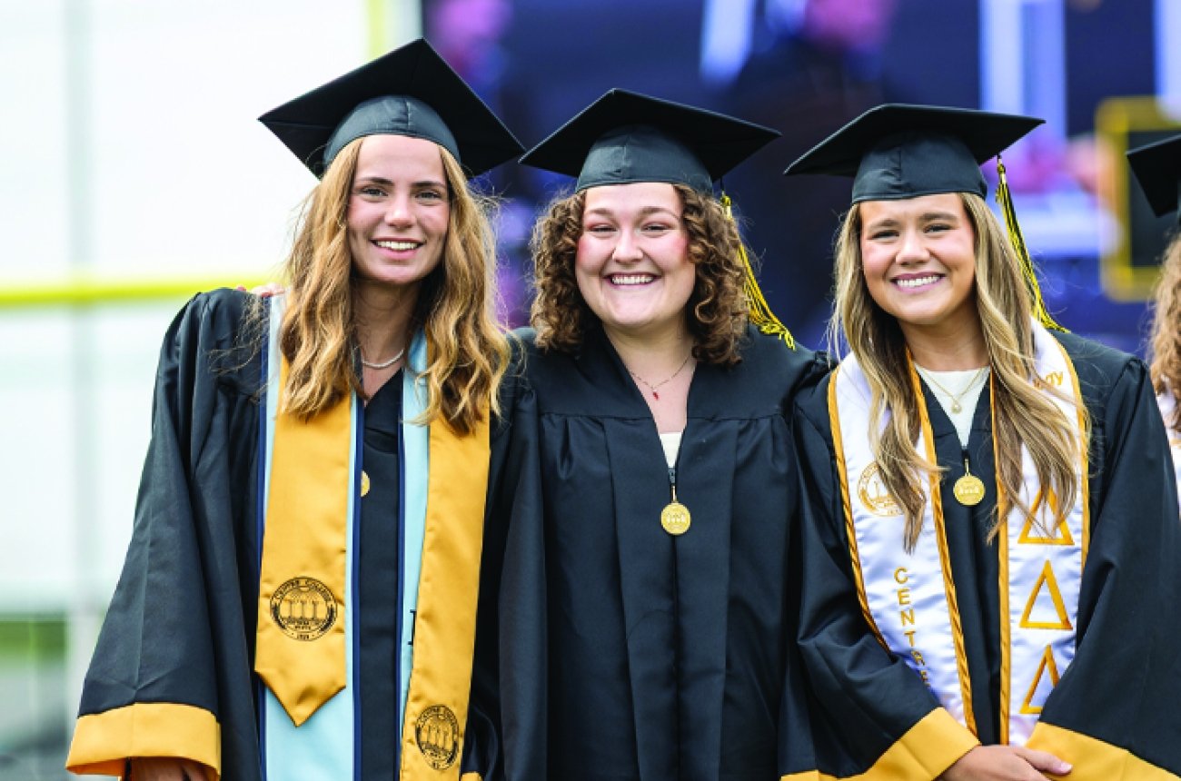 group of students in caps &amp; gowns smiling at photographer at graduation