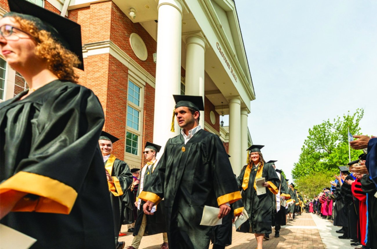 Students wearing caps &amp; gowns walking in front of the library