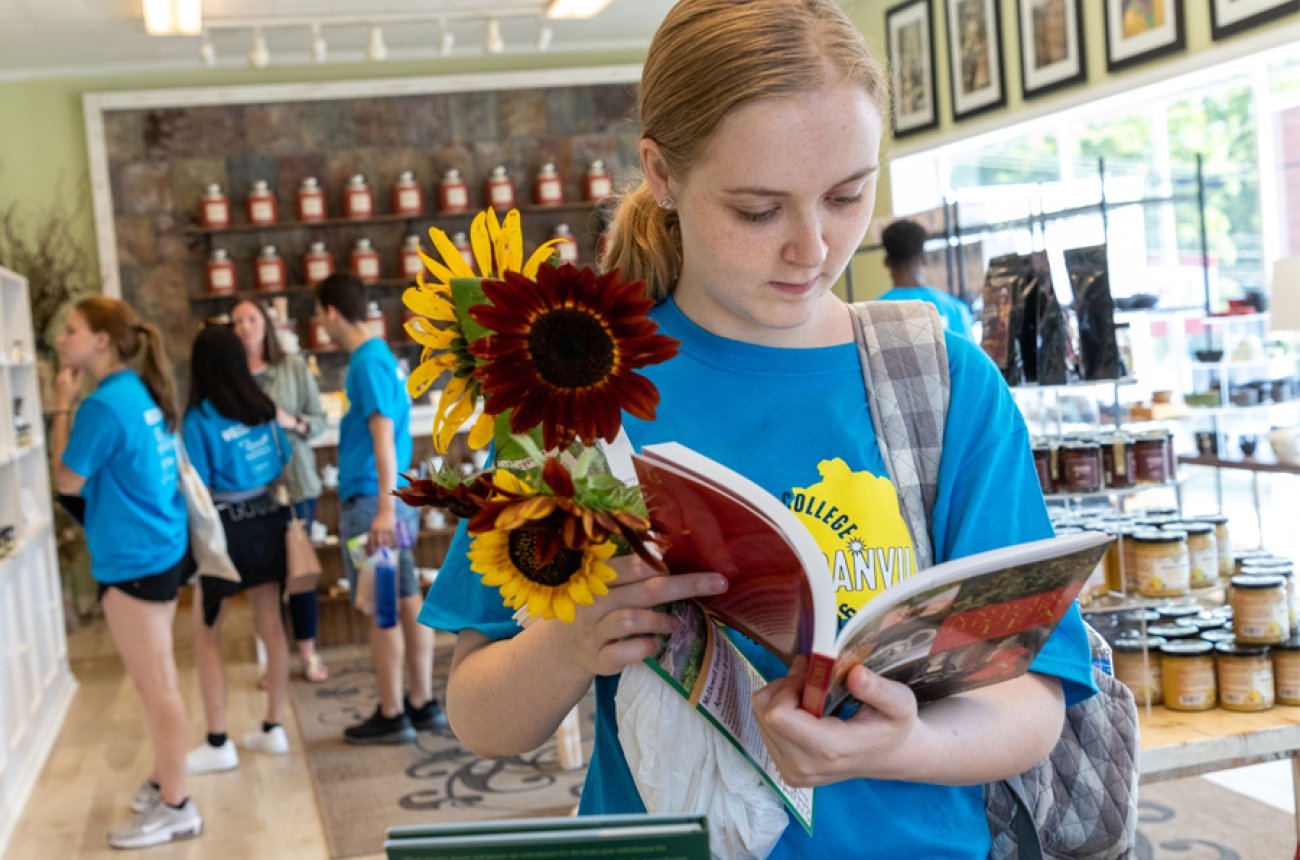 Student holding fresh sunflowers while looking through a book at the local tea shop