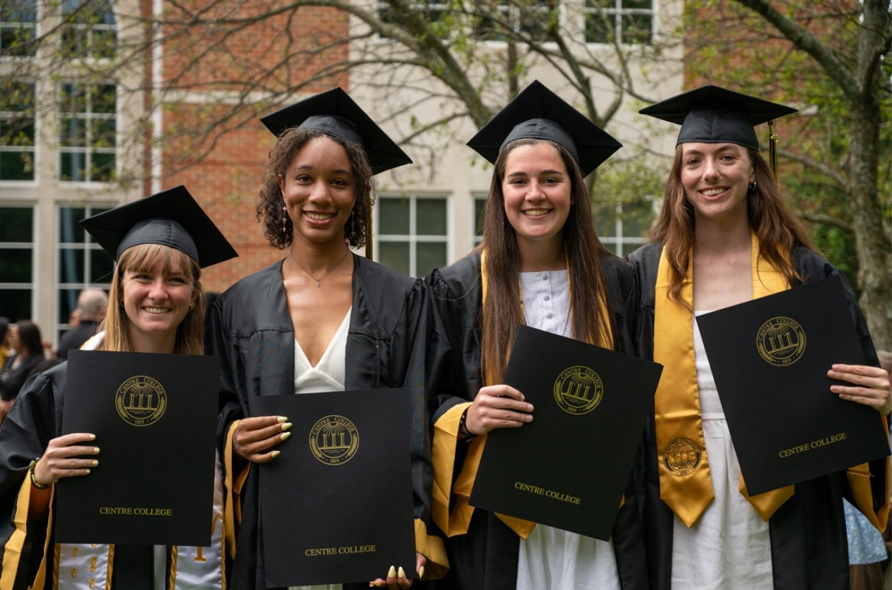 Group of students standing in cap and gown at graduation posing for a photo