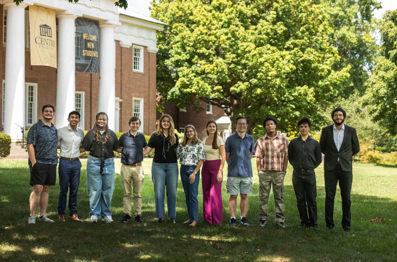 Eleven students standing in a horizontal line smiling at photographer