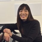 Person smiling while seated next to piano