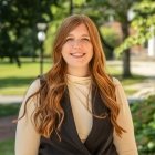 Staff member wearing beige top with black vest standing outside and smiling