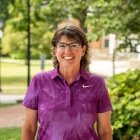 Person wearing purple polo shirt and glasses and smiling at camera
