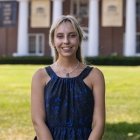 Person wearing blue top and necklace and smiling at camera