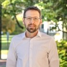 Person wearing button up dress shirt and glasses with beard and smiling at photographer