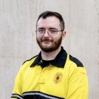 Person wearing glasses and gold and black polo with DPS badge on shirt
