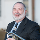 Person smiling while holding trumpet under their arm