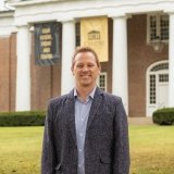 Person wearing sports jacket and dress shirt standing outside the front of Old Centre