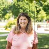 Lady with shoulder length dark hair wearing peach polo shirt standing outside