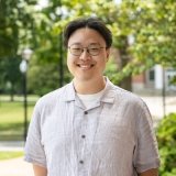 Person wearing button up short sleeve shirt with glasses, and smiling at camera