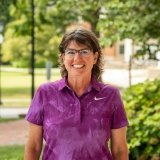 Person wearing purple polo shirt and glasses and smiling at camera