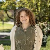 Person wearing cardigan with dress and smiling at photographer