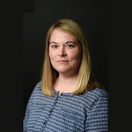 Lady with dark blonde hair wearing blue paisley button up top in front of black background