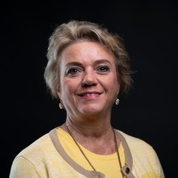 Lady with short light brown hair wearing yellow cardigan and yellow top in front of black background