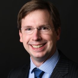 Thomas Allen - man with dark hair wearing glasses and black suit, blue gingham shirt, and navy tie